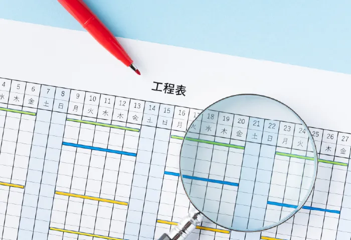 工程表を虫眼鏡と赤ペンで確認する様子